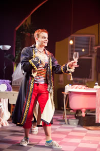 Jerry, with a French regal coat over his stripped tanktop and red pans, holds out an empty wine glass with an effete manner, while in the background we see his shawl-covered dressing table, a pink bathtub, and the apartment's window. 